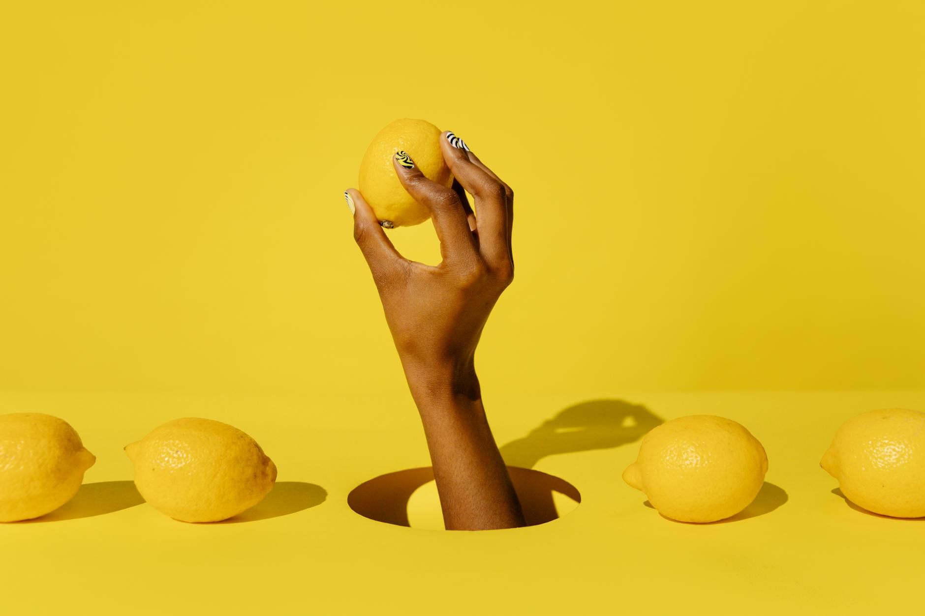 A hand holding a fresh lemon against a bright yellow background, symbolizing renewed vitality and pleasure