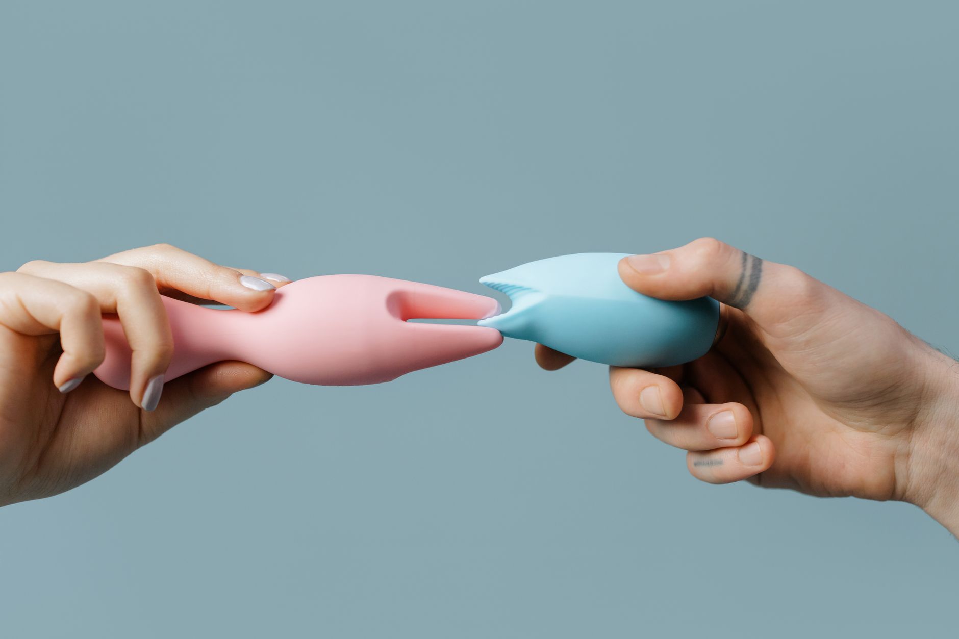Hands holding silicone lemon clitoral vibrators in pastel colors against neutral background
